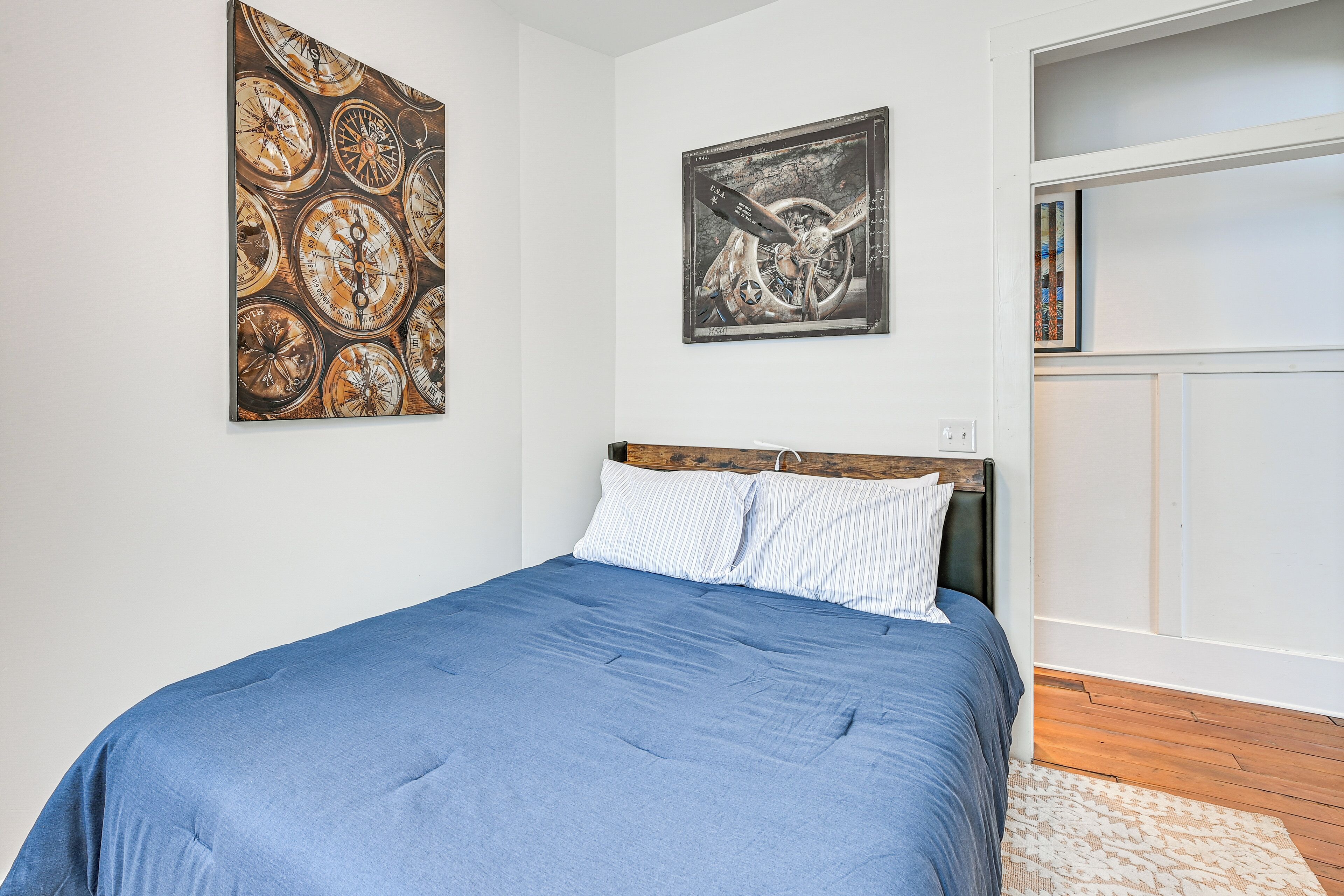A bedroom with a blue bedspread, a wooden headboard, and two wall-mounted artworks.