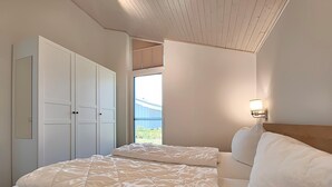 A bedroom with two beds, a wardrobe, and a window with a view of a blue building. - Ferienhaus mit Sauna im Ferienpark Mirow (Mirow)