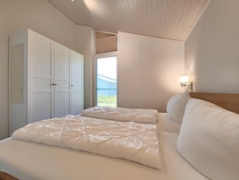 A bedroom with two beds, a wardrobe, and a window with a view of a blue building.