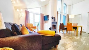 A modern living room with a sofa, chairs, a dining table, and a fireplace. - Ferienhaus mit Sauna im Ferienpark Mirow (Mirow)