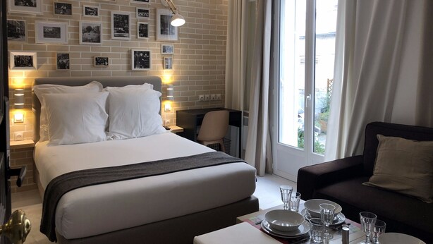Une chambre d’hôtel avec un grand lit, un canapé, une table à manger avec des assiettes et des verres, et un mur décoré de photos encadrées.