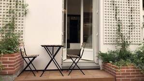 Un petit espace extérieur aménagé avec une table et des chaises, un jardin en briques orné de plantes et un mur blanc à motifs géométriques.