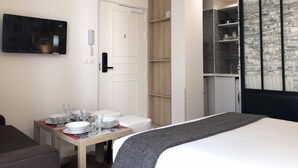 Une chambre d’hôtel comprenant un lit, une table à manger dressée avec des assiettes et des verres, un téléviseur fixé au mur, une armoire en bois et une étagère contenant des ustensiles de cuisine.