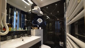 A modern bathroom with a white sink, glass shower enclosure, and a black marble backsplash.
