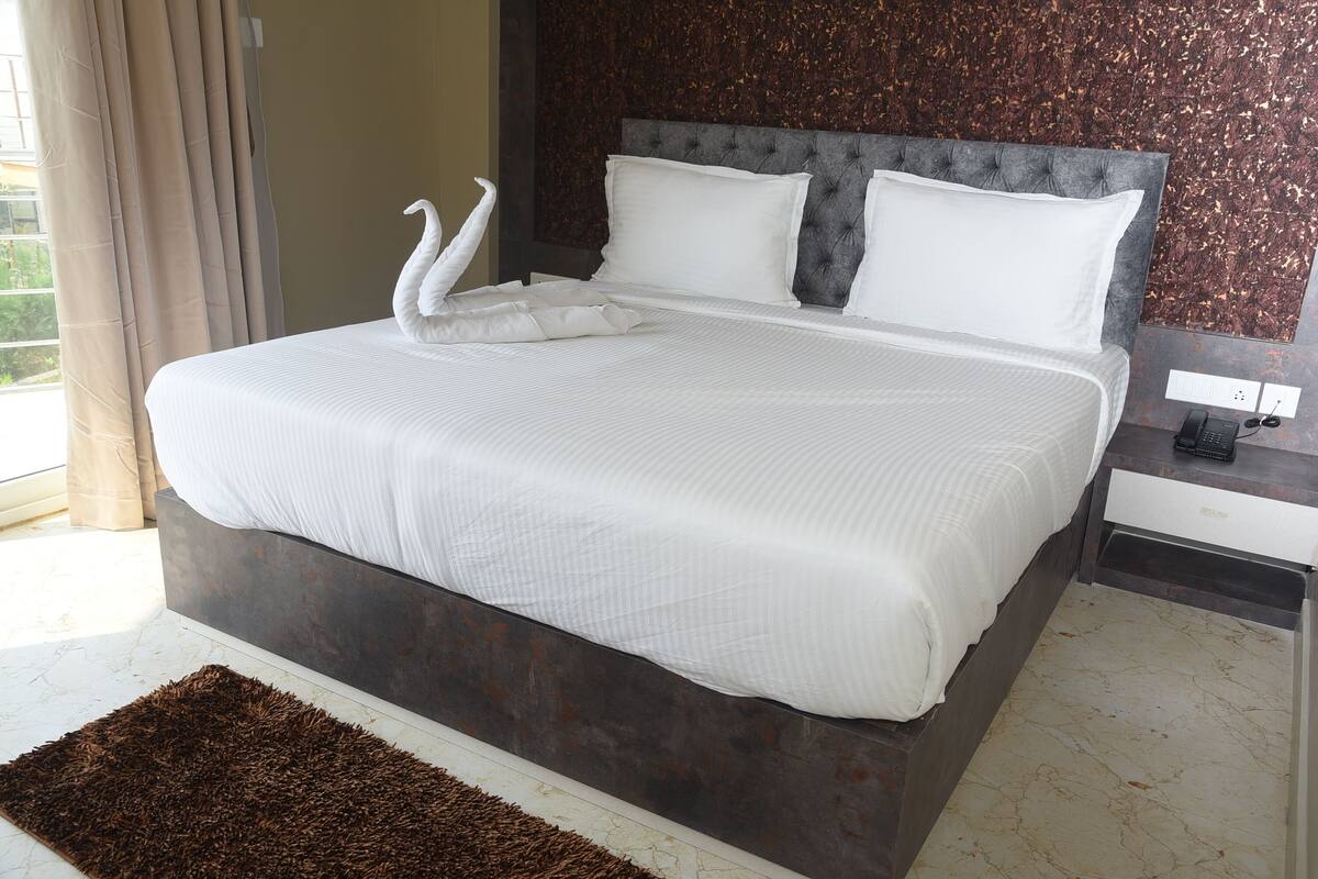 A neatly made bed with white linens and two swan-shaped pillows, a dark headboard, and a marble-patterned wall.