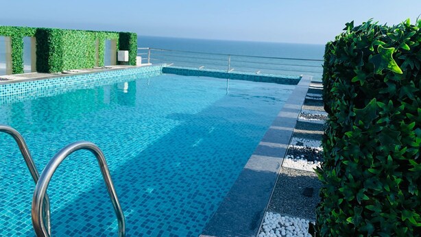 An infinity pool with clear blue water, a metal pool ladder, and a view of the ocean. - The Bay Suite (Brahmagiri)