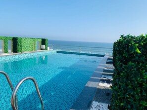 An infinity pool with clear blue water, a metal pool ladder, and a view of the ocean. - The Bay Suite (Brahmagiri)