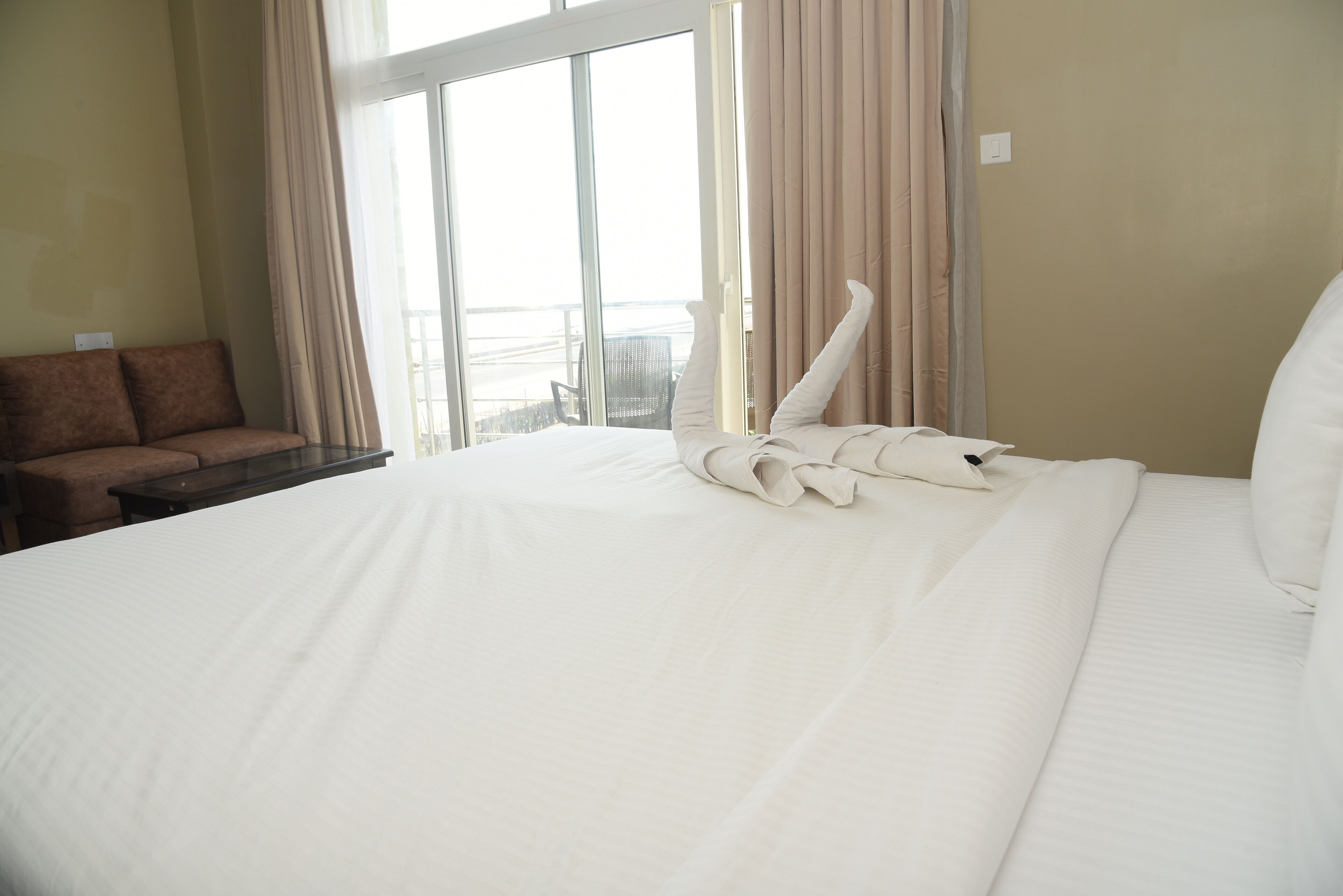 Quarto de hotel com uma cama grande, um sofá marrom e uma janela com cortinas.