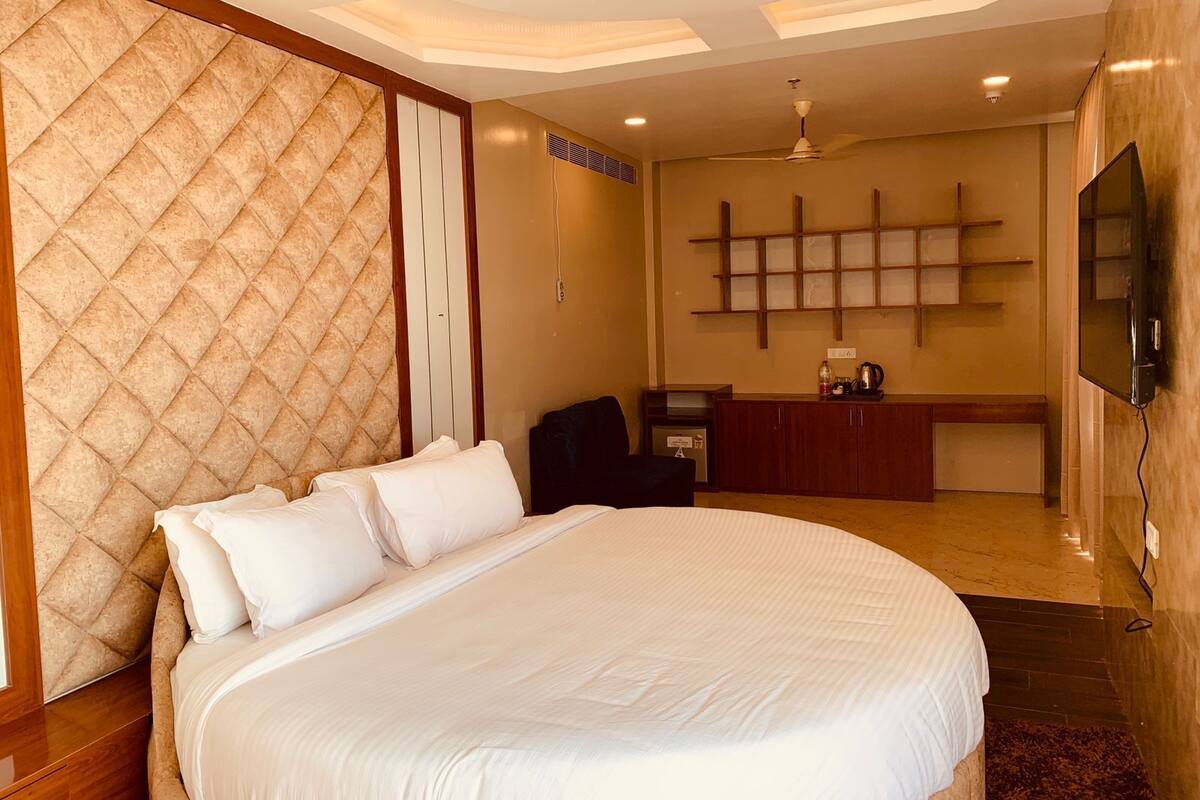 A hotel room with a large bed, a desk with a chair, a TV mounted on the wall, and a ceiling fan.