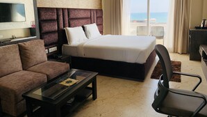 A hotel room with a bed, a sofa, a coffee table, a TV, and a view of the sea. - The Bay Suite (Brahmagiri)