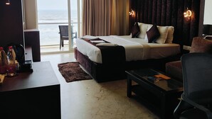 A hotel room with a large bed, a desk, a chair, and a view of the ocean. - The Bay Suite (Brahmagiri)
