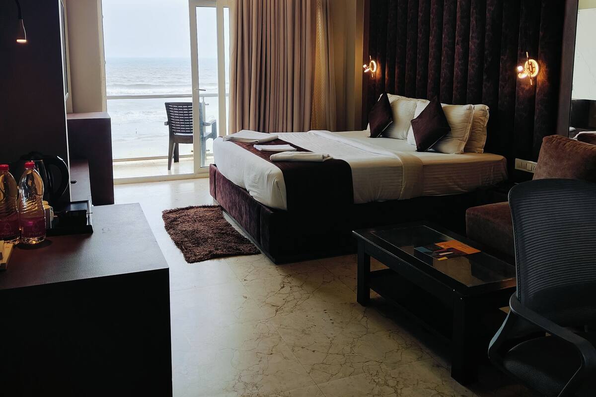 A hotel room with a large bed, a desk, a chair, and a view of the ocean.