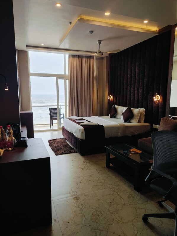 A hotel room with a large bed, a desk, a chair, and a view of the ocean. - The Bay Suite (Brahmagiri)