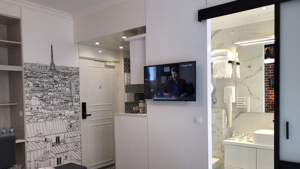 Ein modernes Hotelzimmer mit Essbereich, einem an der Wand befestigten Fernseher und einem Stadtbild-Wandgemälde.