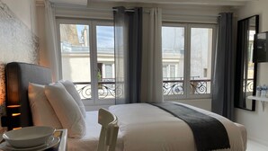 Une chambre d’hôtel avec un lit, une chaise, un bureau avec un bol, et une vue sur le balcon extérieur.