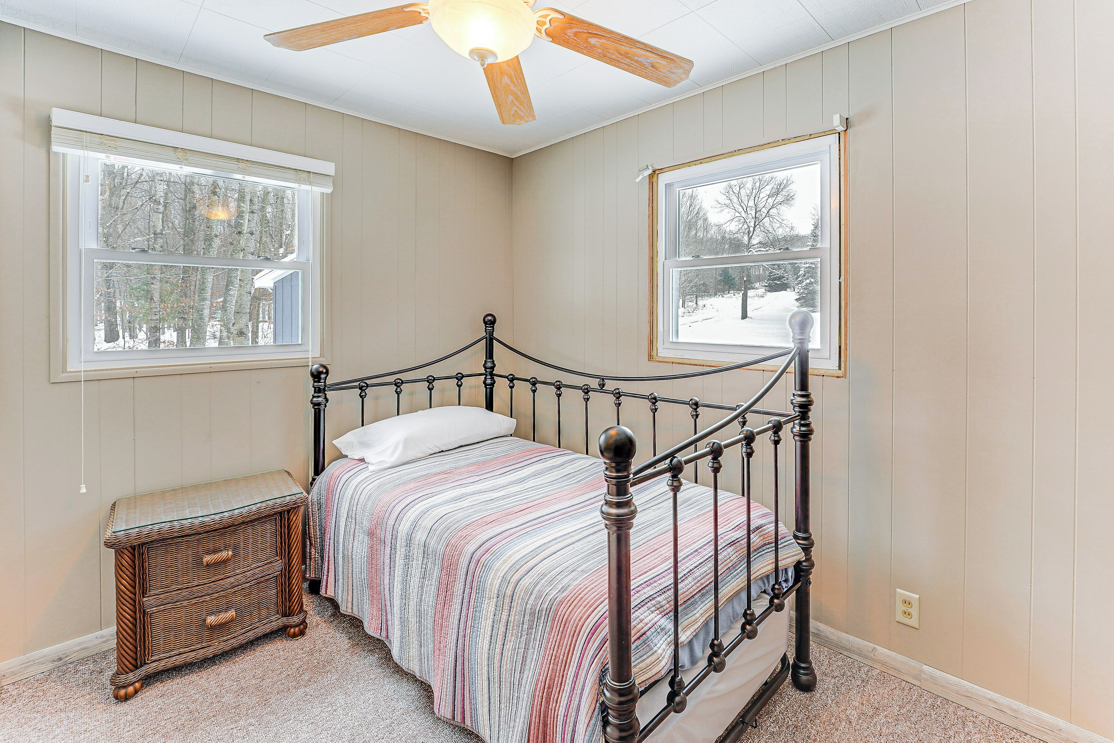 A bedroom with a bed, a nightstand, two windows, and a ceiling fan.