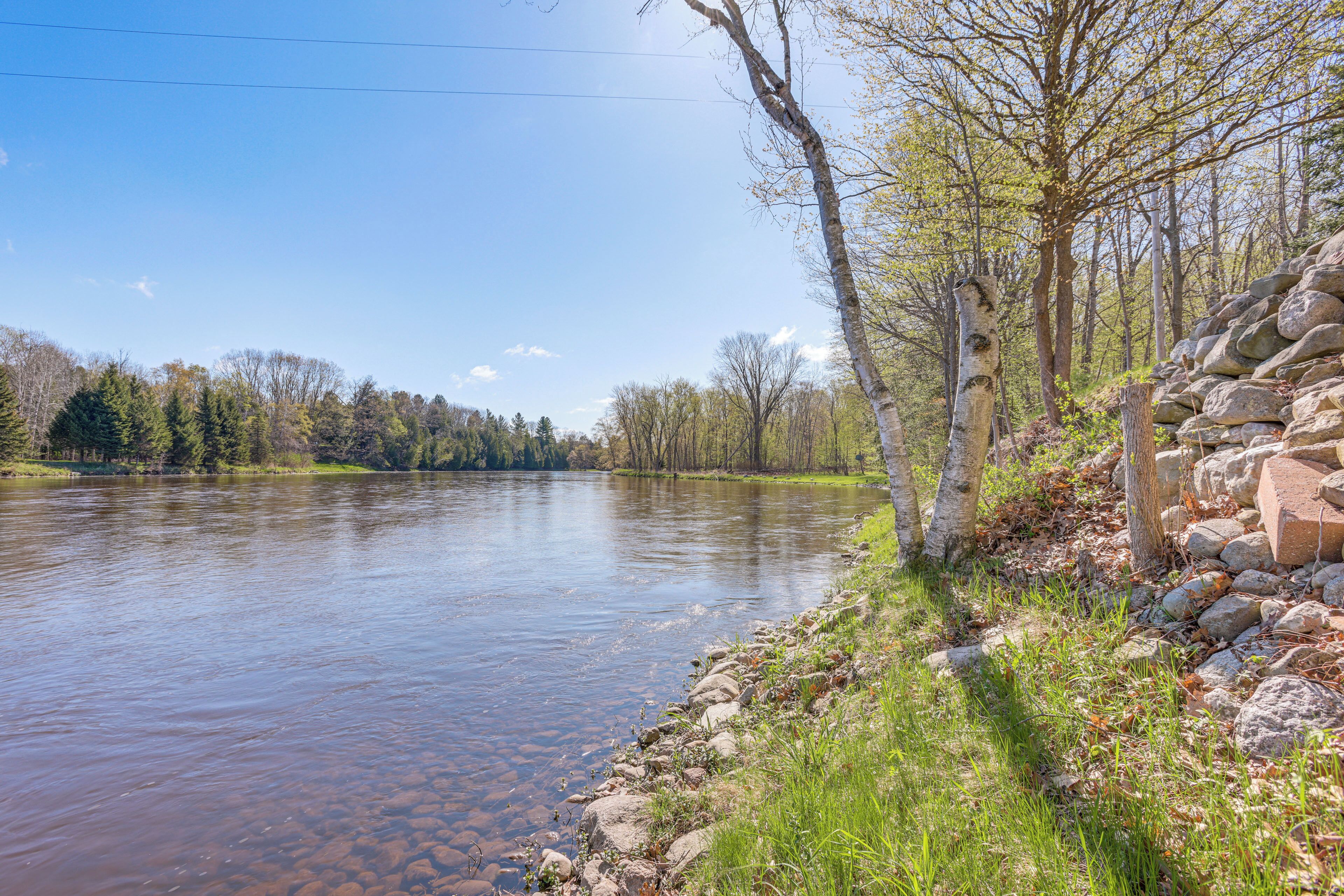 A river with clear water, surrounded by trees and a stone wall.