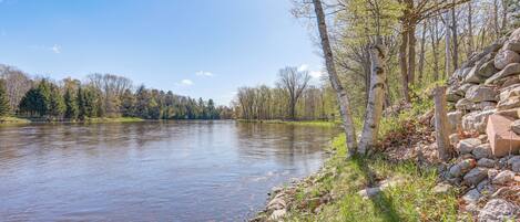 A river with clear water, surrounded by trees and a stone wall.