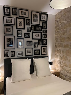 A hotel room with a bed, white pillows, a headboard, and a wall adorned with framed black and white photographs. - Loft Jaures (París)