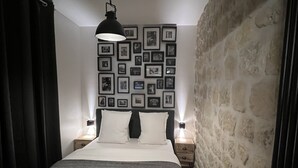 A bedroom with a large bed, two bedside tables, a wall of framed pictures, and a stone wall on one side. - Loft Jaures (París)