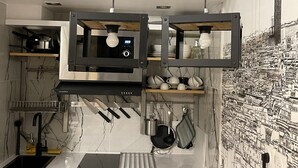 A modern kitchen with a built-in microwave, hanging knives, and a backsplash with a cityscape mural. - Loft Jaures (París)