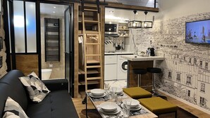 A compact living space with a sofa, dining table set, kitchen area, and a cityscape mural. - Loft Jaures (París)
