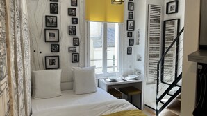 A bedroom with a bed, a desk, and a chair. There are multiple framed pictures on the wall.