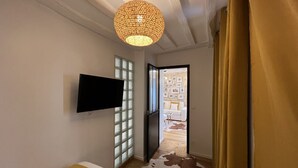 Habitación de hotel moderna con una televisión de pantalla plana montada en la pared, una lámpara de techo con diseño y vistas al área de estar a través de un vidrio.