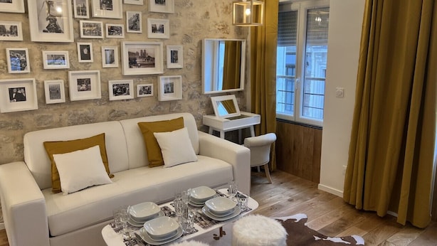 Una sala de estar moderna con un sofá blanco, una mesa de comedor con platos y vasos, y una pared decorada con fotografías enmarcadas.