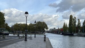 Un paseo a orillas del río con pavimento adoquinado, bancos y farolas.