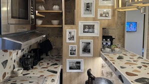 Una cocina con microondas integrado, cafetera y encimera con un diseño de azulejos único. En la pared hay fotografías enmarcadas y un televisor montado sobre la encimera.