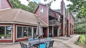 A red building with a covered patio, outdoor seating, and a view of the surrounding trees.
