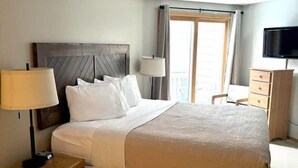 A hotel room with a large bed, bedside lamps, a TV, and a dresser.