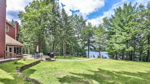 Un espace extérieur verdoyant avec un sentier en pierre, une terrasse en bois et une vue sur un lac.