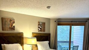 Ein Hotelzimmer mit zwei Betten, einer Deckenleuchte und Blick ins Freie durch ein Fenster.
