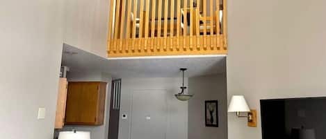 A living room with a ceiling fan, a TV, a dining area, and a staircase to an upper level.