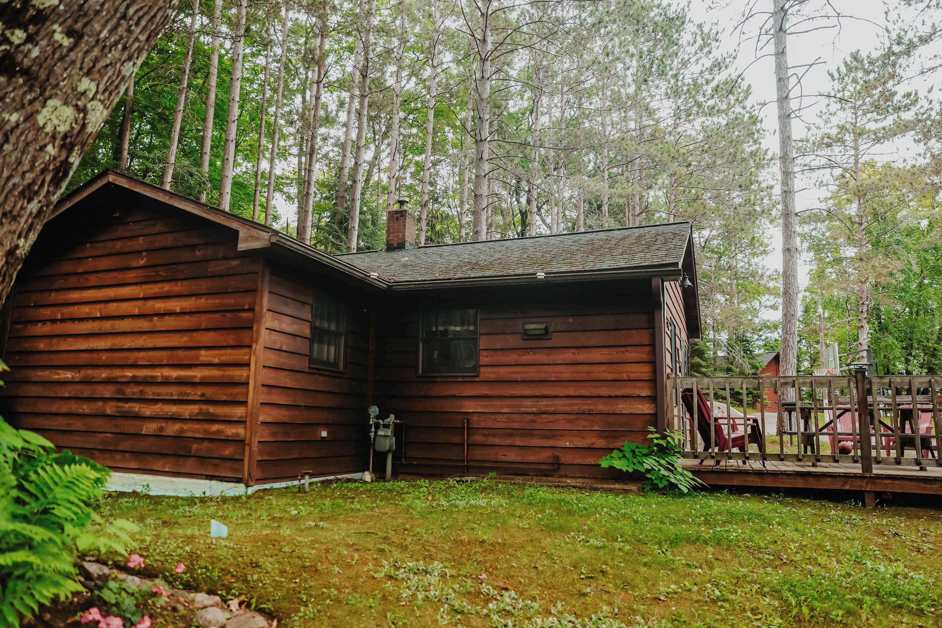 A wooden cabin with a porch, surrounded by a forest.