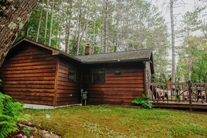 A wooden cabin with a porch, surrounded by a forest.
