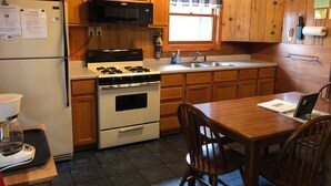 Une cuisine avec des meubles de rangement en bois, une cuisinière, un four à micro-ondes, un évier et une table à manger avec des chaises.