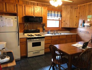 A kitchen with wooden cabinets, a stove, a microwave, a sink, and a dining table with chairs.