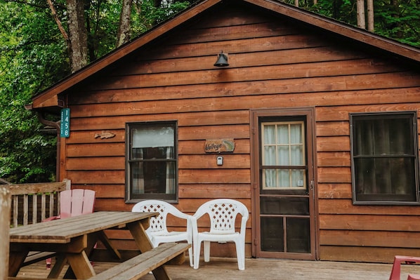 A wooden cabin with a picnic table and two white plastic chairs outside.