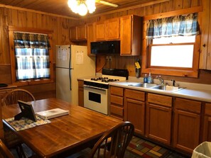 A wooden cabin-style kitchen with a refrigerator, stove, microwave, and sink.