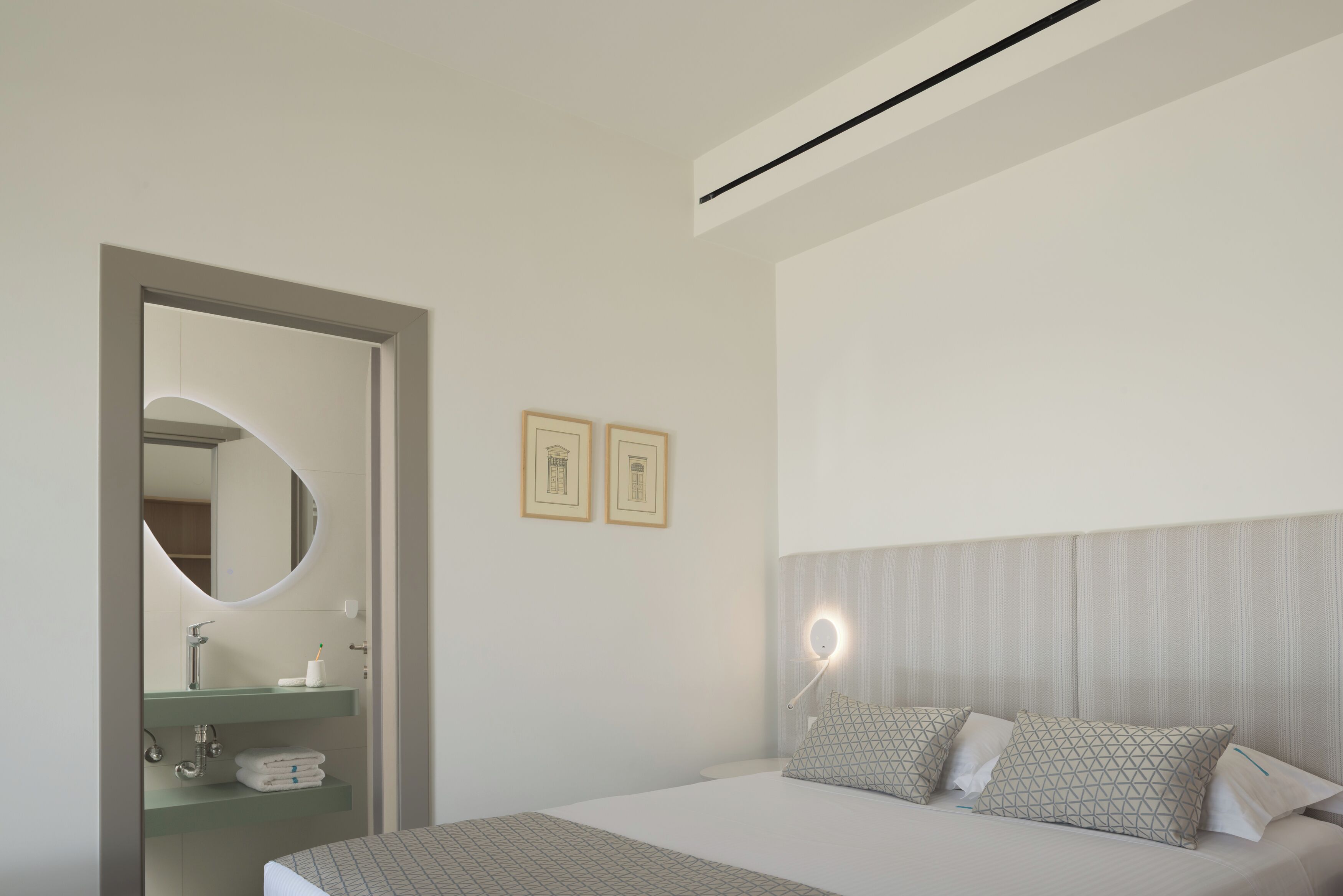 A modern bedroom with a bed, a bedside table, a mirror, and a wall-mounted light fixture.