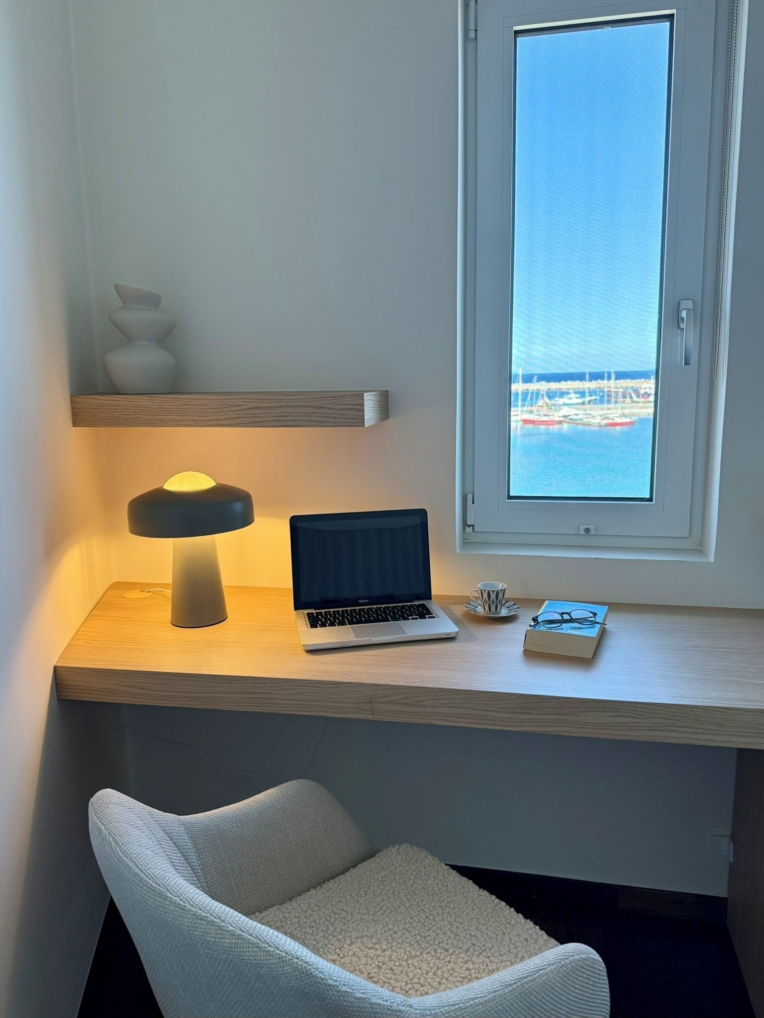 A workspace with a laptop, a lamp, and a view of the sea through a window.