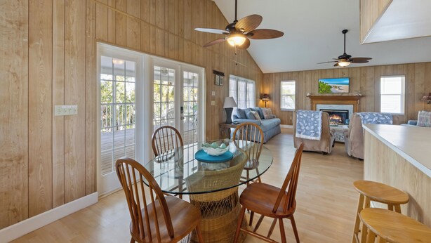 A spacious living area with a glass dining table surrounded by wicker chairs, a fireplace, and a television mounted on the wall. - The Twins: Your Perfect Budget Beach Getaway! (Anna Maria)