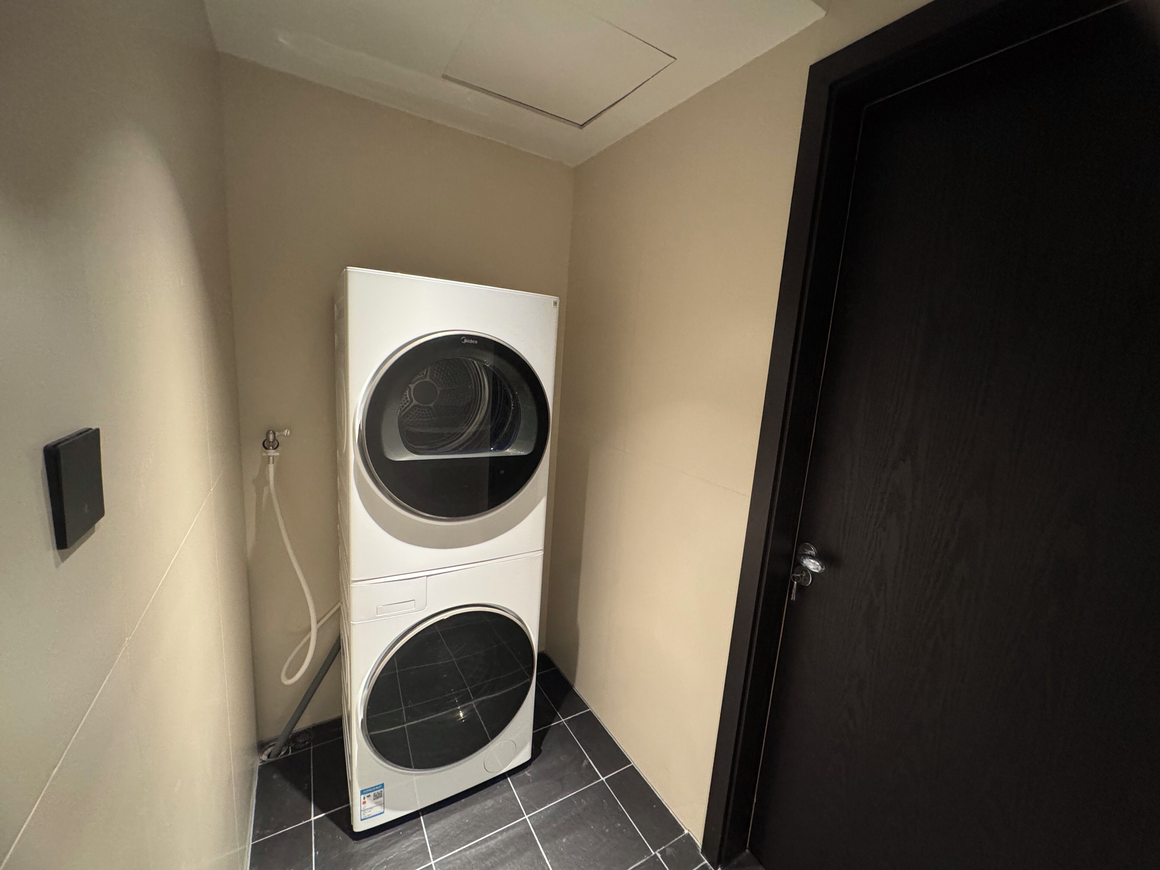 Un lavadero con dos lavadoras apiladas, una puerta y un interruptor de luz en la pared.