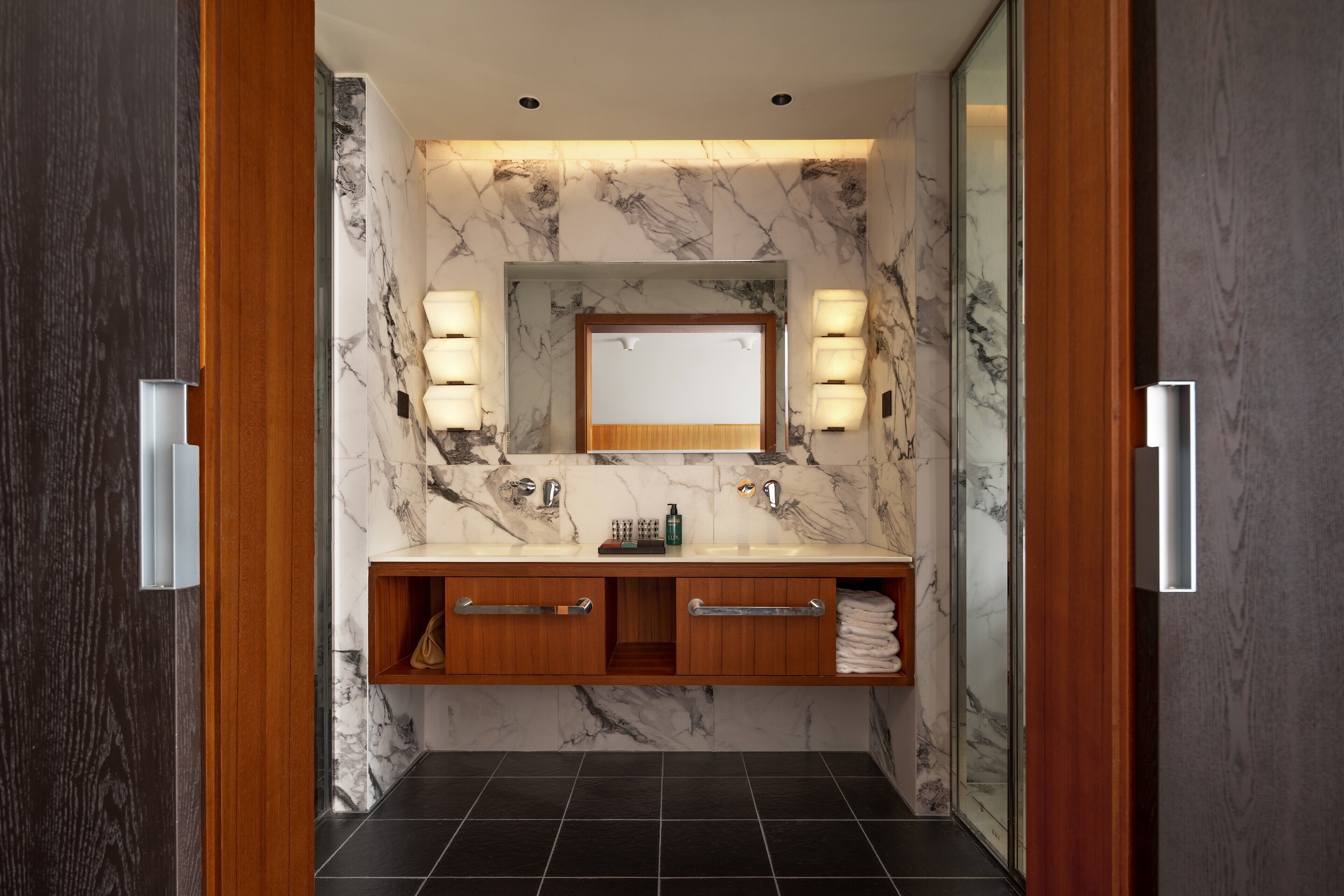 A modern bathroom with a marble backsplash, a central mirror, and dual vanity sinks.
