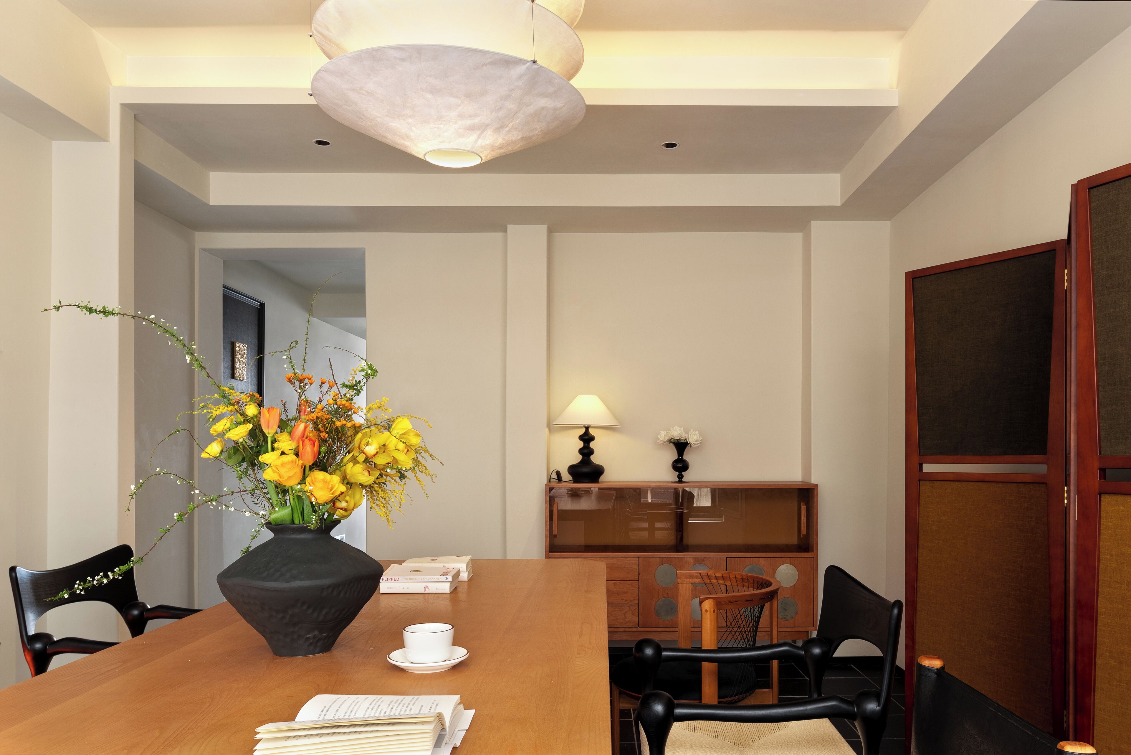 Un comedor con mesa de madera, sillas, un jarrón de flores y una lámpara.