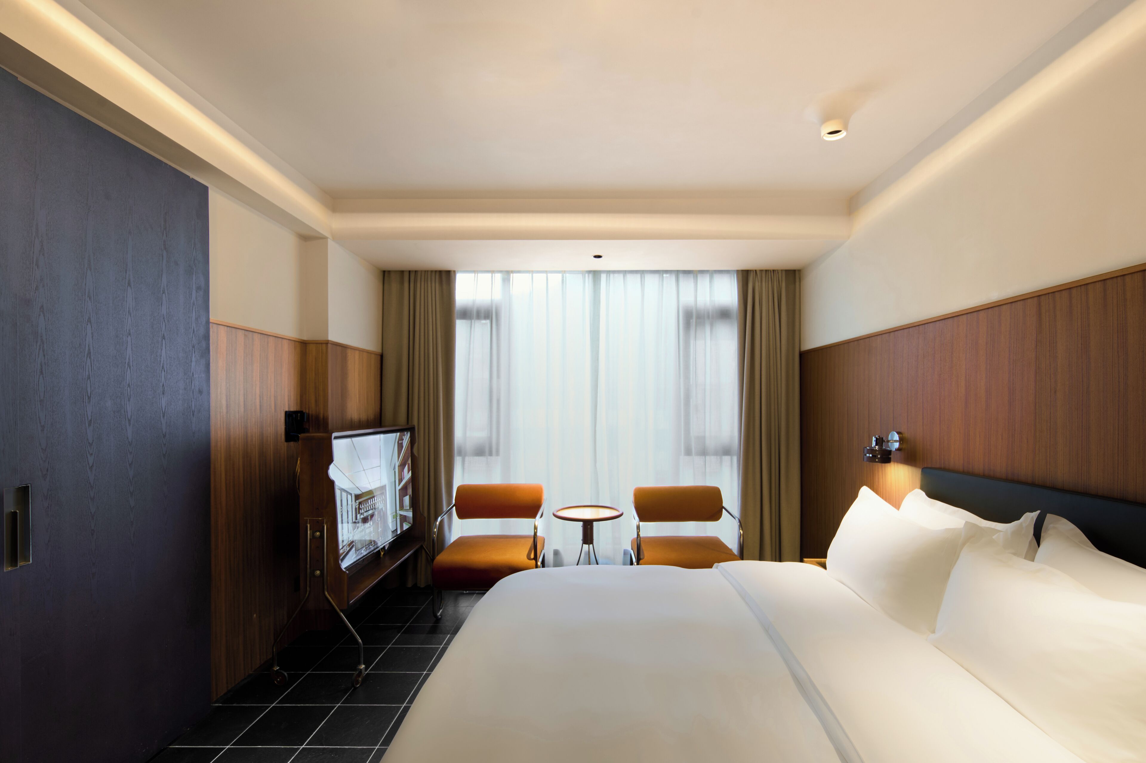 A hotel room with a large bed, two armchairs, a small table, and a TV.