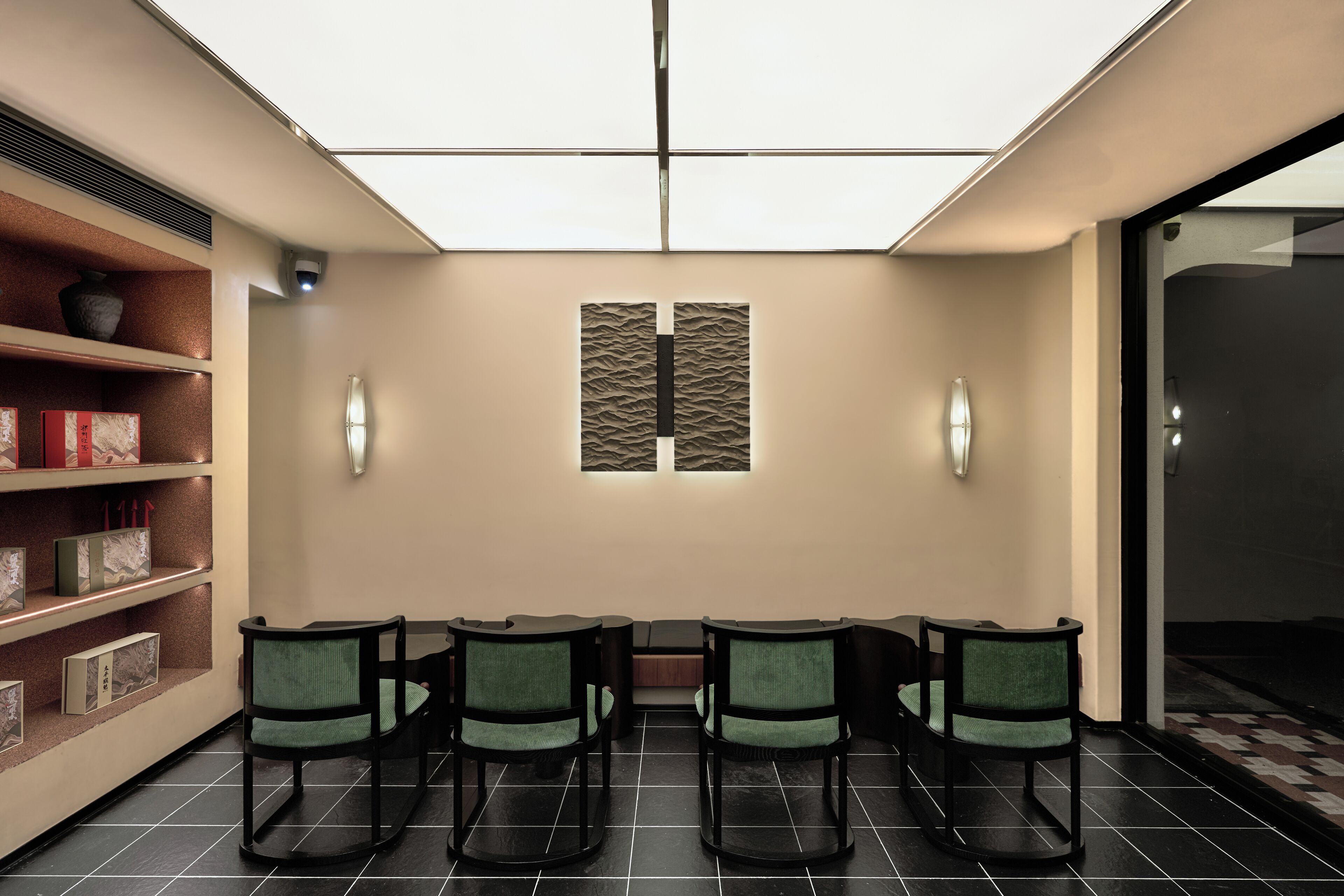 A waiting area with a long bench, four chairs, a bookshelf, and a wall-mounted light fixture.